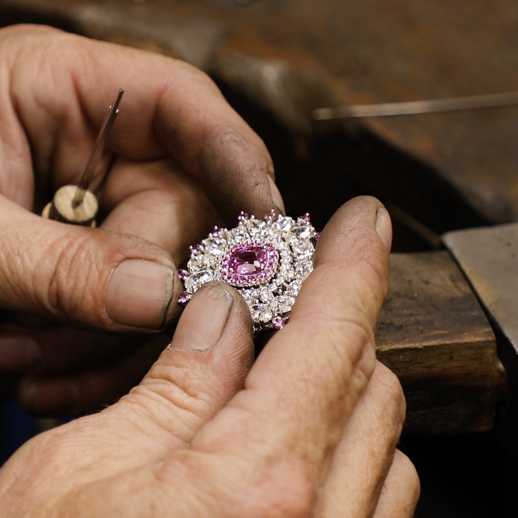 jewellers hands holding pink sapphire and diamond pendant