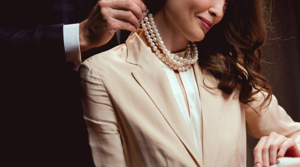 man putting pearl necklace on lady