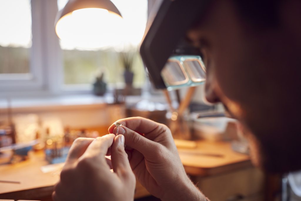 Close Up Of Male Jeweller Looking At Ring Through Headband Magnifiers In Studio