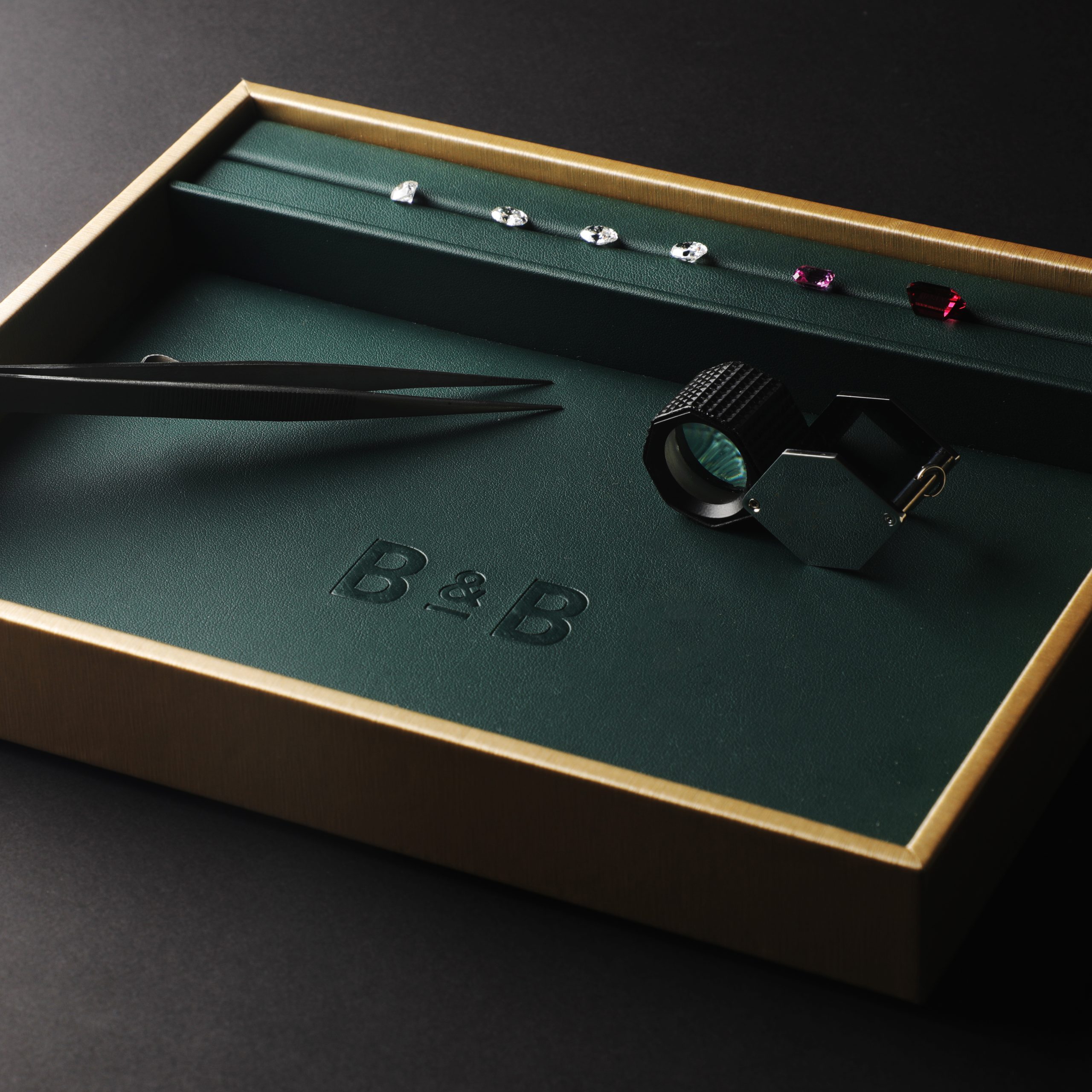 Gemstones and diamonds on a B&B tray with tweezers and loupe