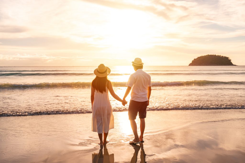 Young woman traveler holding man's hand and looking beautiful sunset on the beach, Couple on vacation in Australia