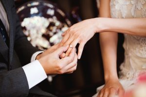 groom putting solitaire engagement ring on bride's hand