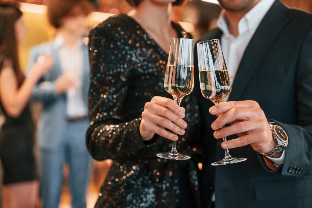 Close up view of champagne glasses. Group of people in beautiful elegant clothes are celebrating engagement