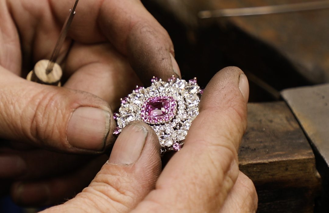 jewellers hands holding pink sapphire and diamond pendant
