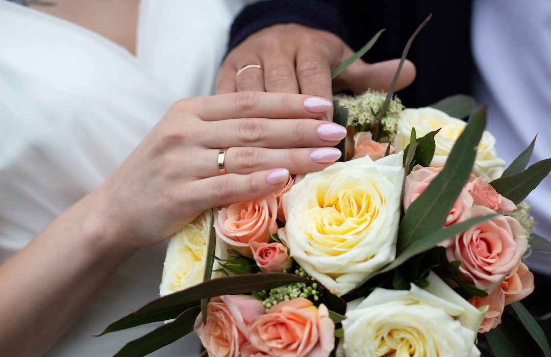 Hands of bride and groom with wedding rings on wedding bouquet