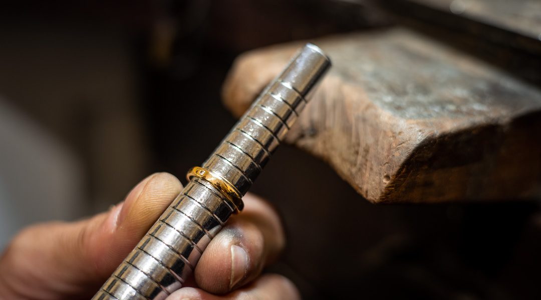 Jeweler hands measuring and checking ring size gauge mandrel. Goldsmith working repairing a gold jewel in his jewelry workshop.