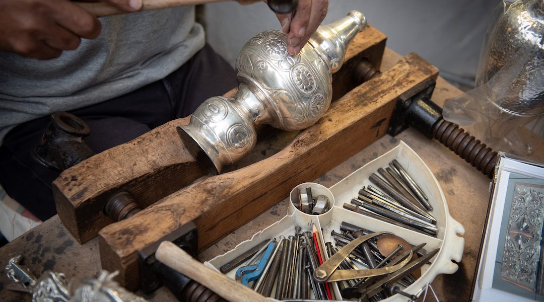 Jewellery maker working in workshop crafting homemade silver vase.