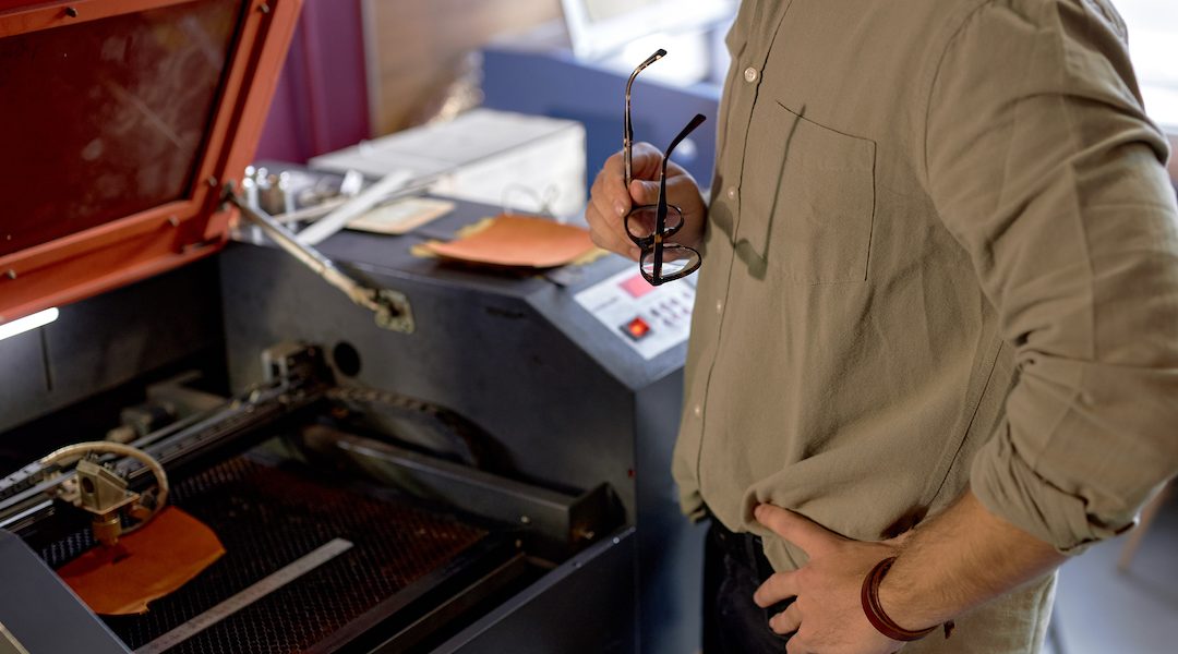 man with hands on the hips watching on laser engraver working, close up side view cropped shot